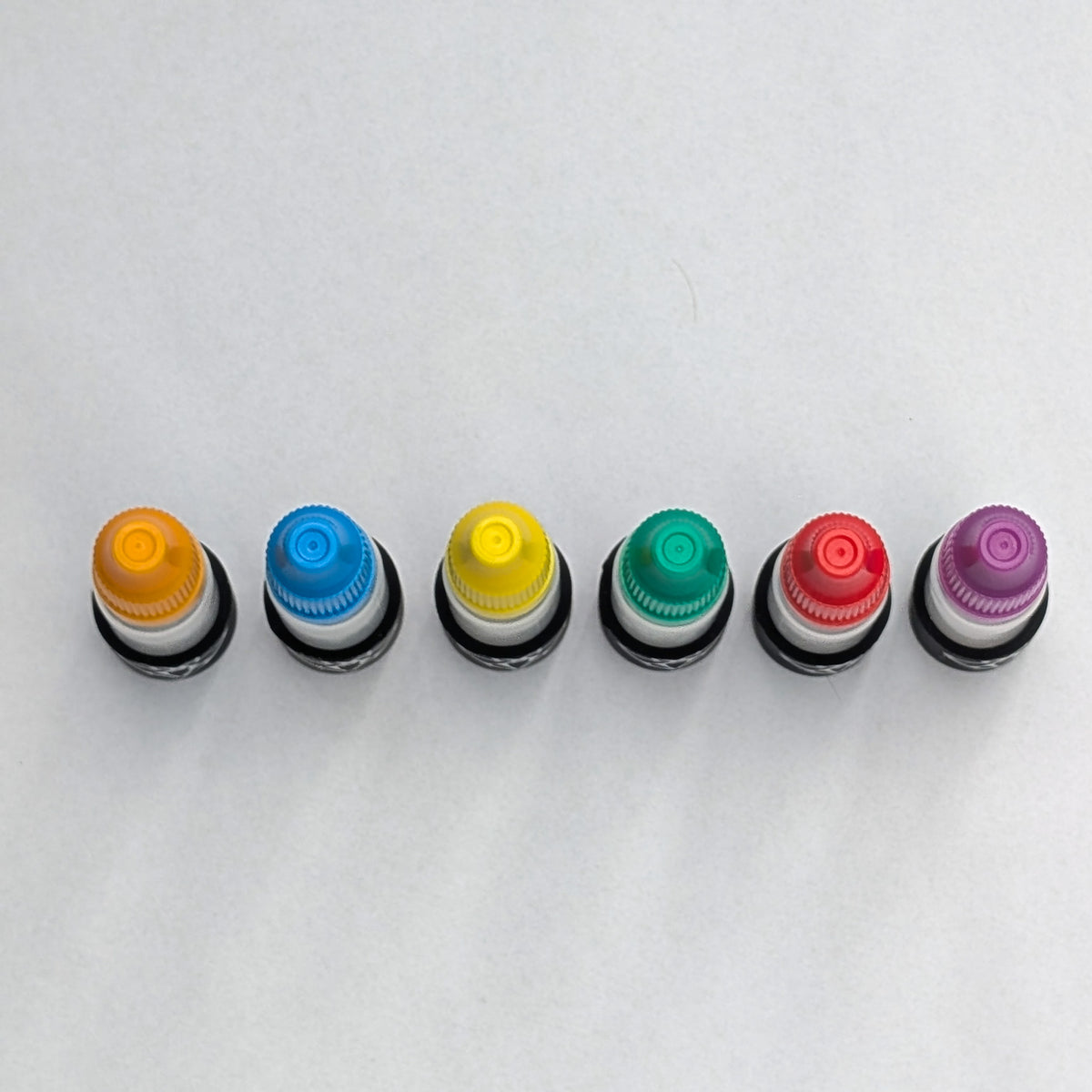 Six magnetic glue bottles from above, showing the coloured cap tops in a row