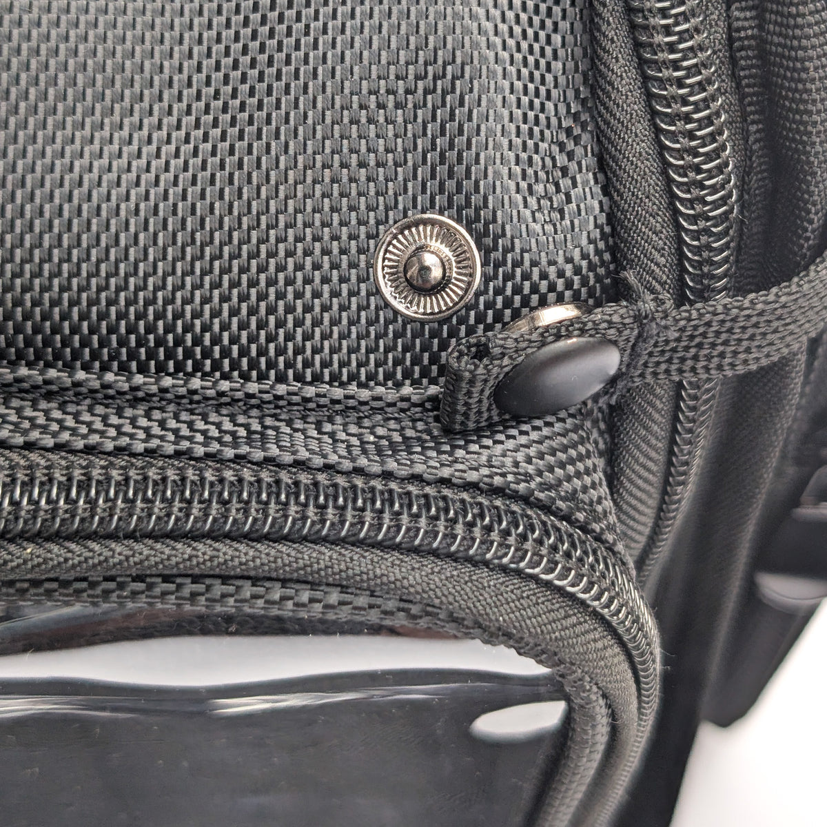 Close-up of a black textured Moth Pro bag with a silver snap button, zipper, and black plastic toggle on a white background.