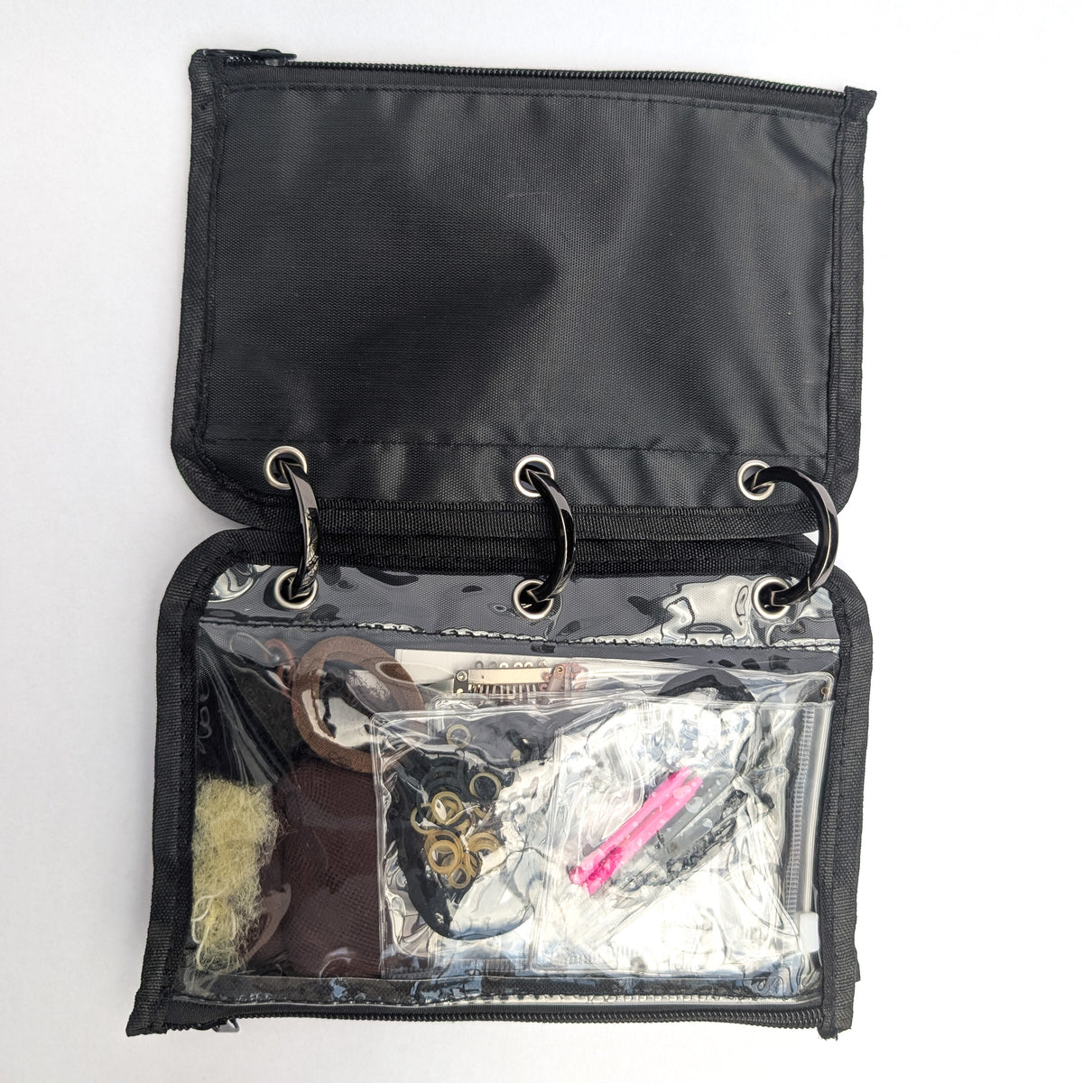 An open black zippered organizer pouch with three metal rings and a clear front pocket containing various small accessories, photographed on a white background.