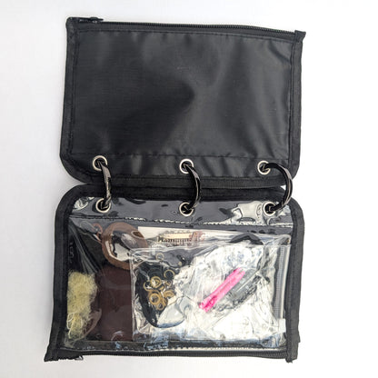An open black zippered organizer pouch with three metal rings and a clear front pocket containing various small accessories, photographed on a white background.