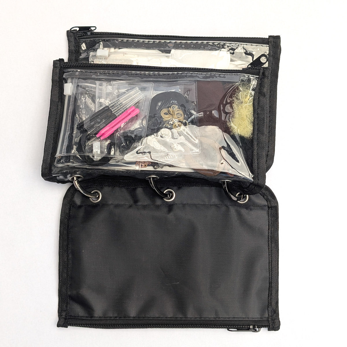 A black nylon makeup organizer pouch shown open on a white background, revealing a clear front pocket filled with cosmetics and a black zip section behind it.