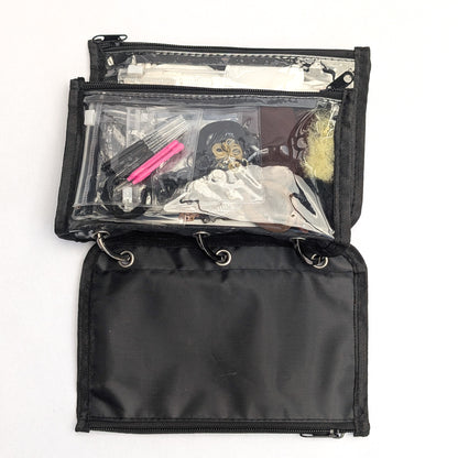 A black nylon makeup organizer pouch shown open on a white background, revealing a clear front pocket filled with cosmetics and a black zip section behind it.
