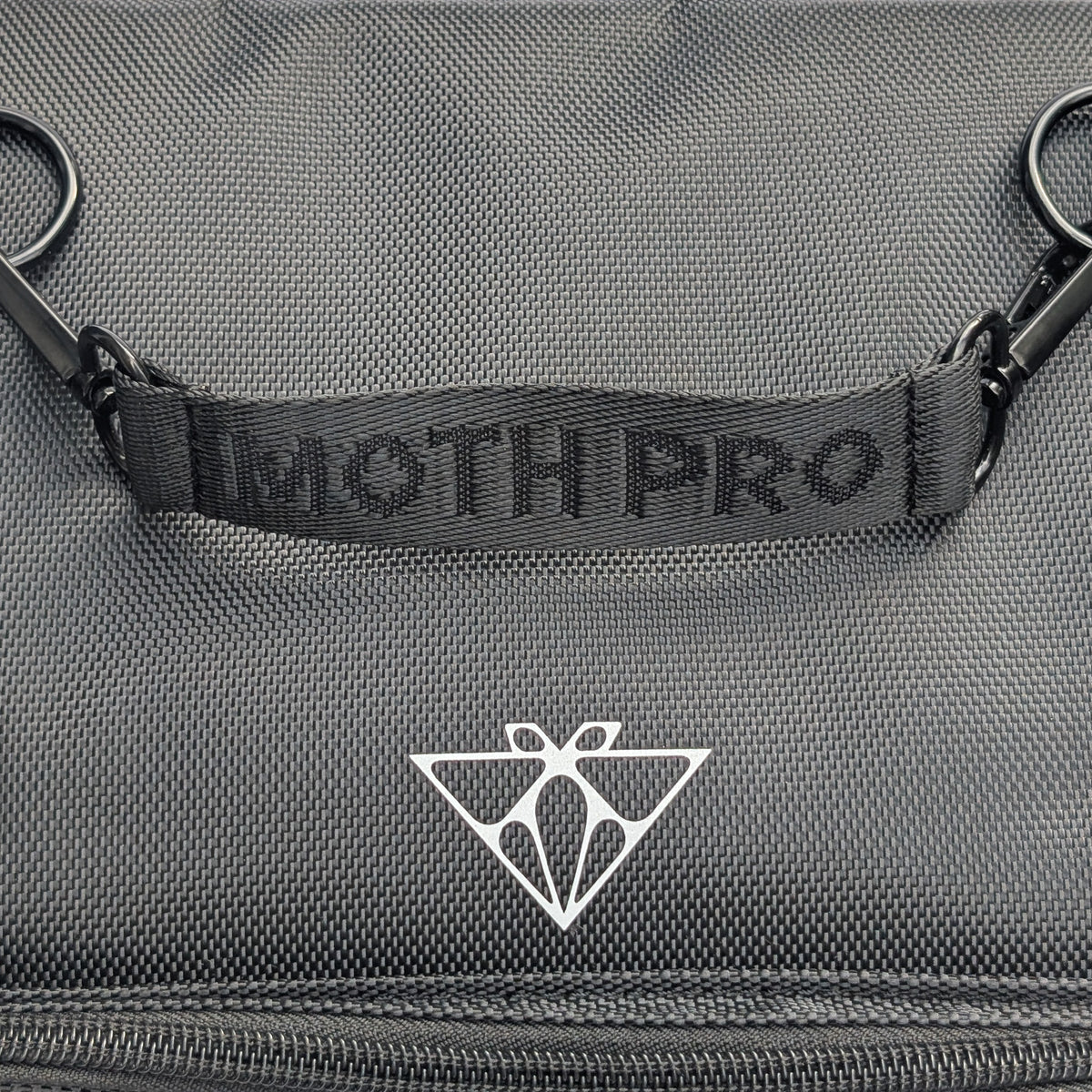 Close-up of a dark gray textured fabric bag with a black webbed handle embossed with 'MOTH PRO' and a white geometric Moth Makeup logo below it.