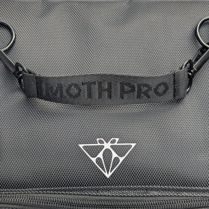 Close-up of a dark gray textured fabric bag with a black webbed handle embossed with 'MOTH PRO' and a white geometric Moth Makeup logo below it.